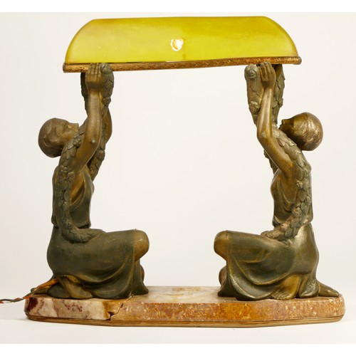 213 - A French Art Deco cold painted table lamp, two ladies holding a green glass canopy above, raised on ... 