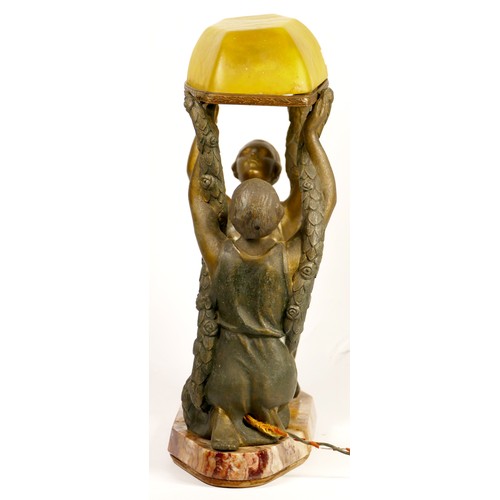 213 - A French Art Deco cold painted table lamp, two ladies holding a green glass canopy above, raised on ... 