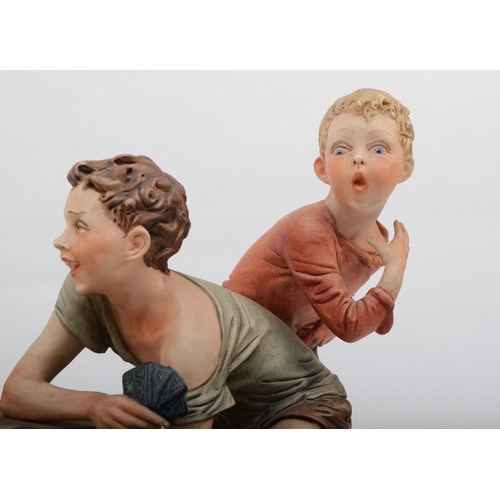 150 - A 20th century Capodimonte porcelain figure, The Cheats, modelled by B.Merli, raised on an oval wood... 