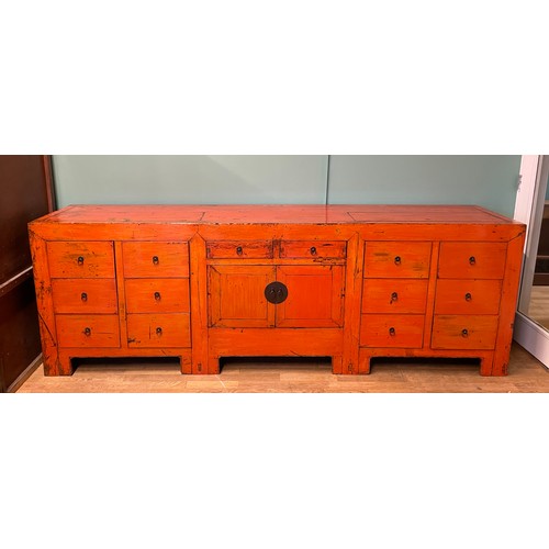 A large contemporary Chinese red lacquered sideboard, comprising of two short central drawers over fitted cupboard, flanked by six deep drawers, with burnished brass drop loop handles, raised on bracket supports, W265, H89, D59cm.