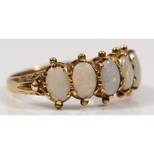 106 - A 9ct gold five stone opal dress ring, with pierced scrolling shoulders, the opals showing flashes o... 