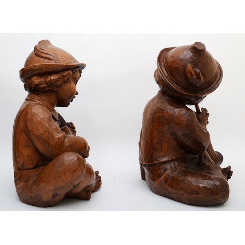 244 - A rare pair of carved wood Hummel figures, presumed ex shop display, of seated boys playing musical ... 