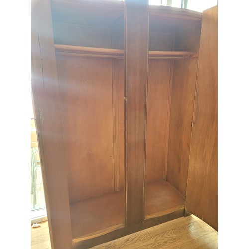 160 - A mid 20th century walnut veneered double wardrobe, the curved double doors opening to a fitted rail... 