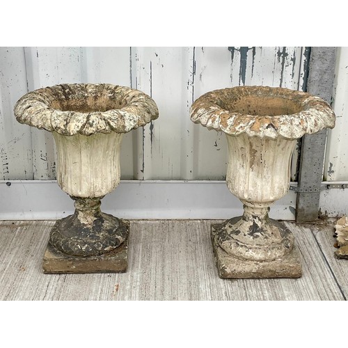 412 - A pair of reconstituted stone leaf urns, raised on square bases, 61cm