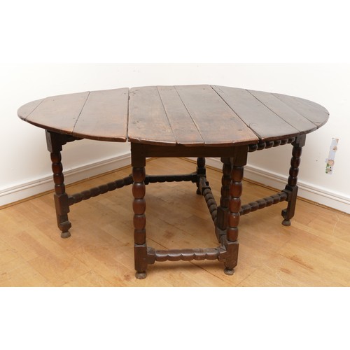 494 - A 17th century oak drop leaf dining table, the oval top raised on turned supports with double gate-l... 