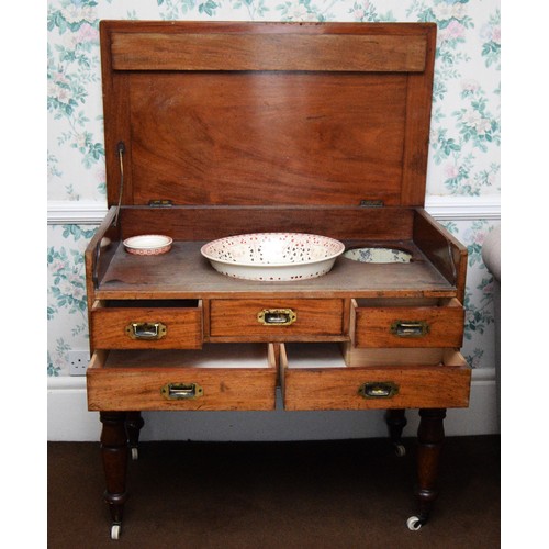 A 19th century mahogany campaign washstand, the hinged lid opening to reveal a tin lined wash bowl, soap dish and water jug holders over three short drawers (central a dummy) over two long drawers, removable turned legs with porcelain castors