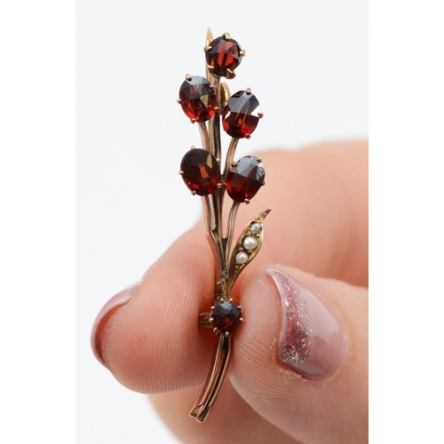 100 - A 9ct gold seed pearl and garnet brooch, shaped as a small bunch of flowers, sixe garnets of varying... 