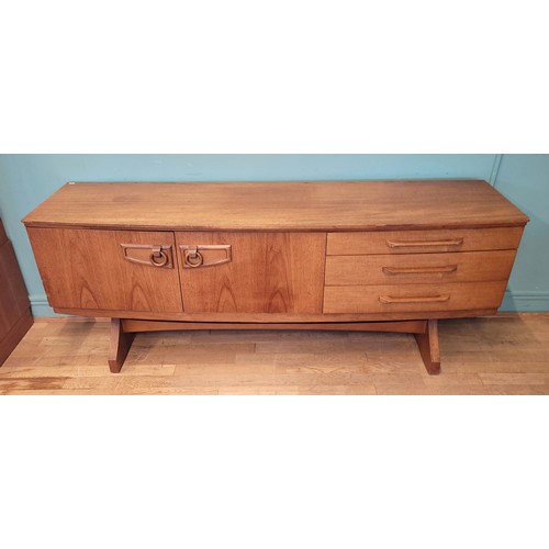 Beautility: A mid 20th century teak sideboard credenza/drinks cabinet, of rectangular form with shallow concave front, a central fall front cabinet door, flanked by a cupboard, and a bank of three graduated drawers, having carved wooden ring handles, raised on square supports, with central scretcher, W184, D48, H74cm.