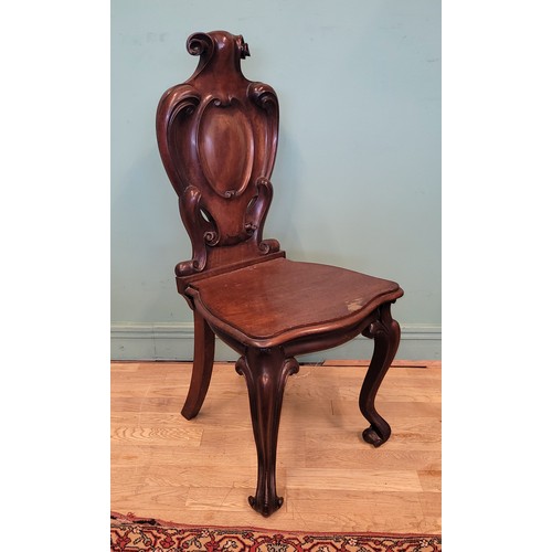 378 - A Victorian mahogany hall chair, the deeply carved scroll back with solid seat, raised on cariole le... 