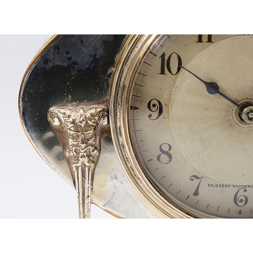 12 - An oval hammered Arts and Crafts silver plated desk clock, raised on monopedia supports with satyr h... 