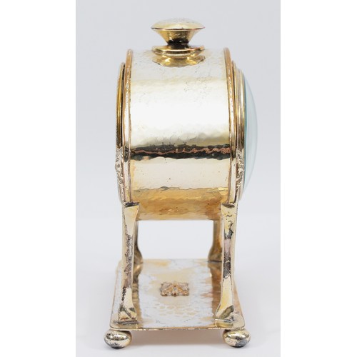 12 - An oval hammered Arts and Crafts silver plated desk clock, raised on monopedia supports with satyr h... 