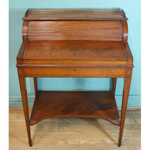 A fine Sheraton Revival satinwood tambour front writing desk, c.1910, of small and elegant proportions, the three-quarter pierced brass gallery above a raised cylinder section, rolling back by opening the frieze drawer (with Hobbs lock) to reveal partitioned letter racks flanking a pen & ink tray over three drawers, with further secret compartments below a lift-out stationary tray, the gently sloped top with Neoclassical embellishments, edged throughout in ebonised stringing, opening to form a baize writing surface, standing on tapered square legs above the concave fronted base shelf and spade feet.
H94, D50, W73cm.