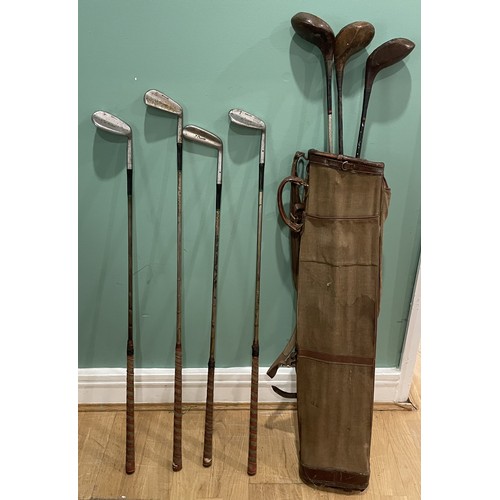 34 - A group of vintage golf clubs, including woods and irons in canvas and leather golf bag.