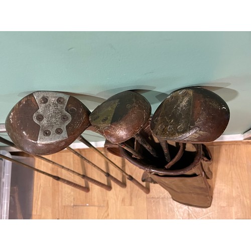 34 - A group of vintage golf clubs, including woods and irons in canvas and leather golf bag.