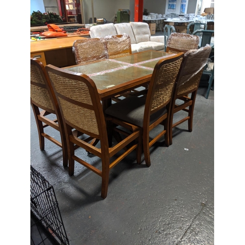 556 - A teak glass topped dining table with 7 rattan back chairs - no seats