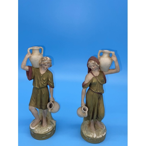228 - A pair of Royal Dux middle eastern water carrier figures both male and female carrying amphoras - 10... 