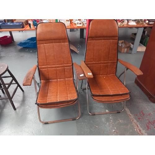 107 - Two tan leatherette folding and reclining armchairs with retractable footrests