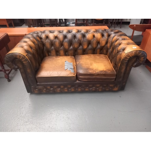 121 - A leather chesterfield two seater sofa (tear to cushion)