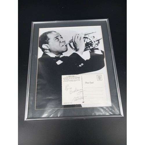 125 - A framed photograph of Louis Armstrong including a hand signed autograph on a postcard