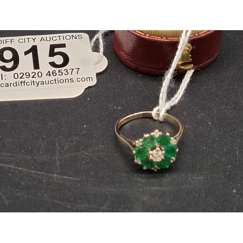 915 - An 18 carat white gold, diamond and emerald cluster ring - a central diamond surrounded by six emera... 