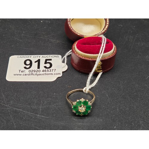 915 - An 18 carat white gold, diamond and emerald cluster ring - a central diamond surrounded by six emera... 