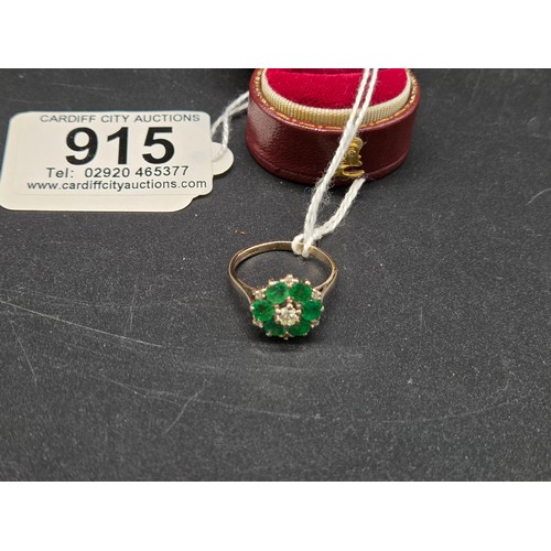 915 - An 18 carat white gold, diamond and emerald cluster ring - a central diamond surrounded by six emera... 