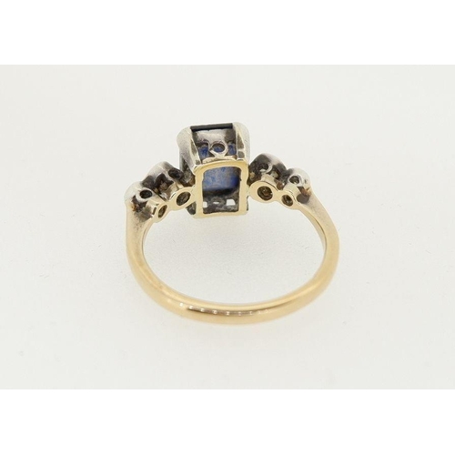 472 - An 18ct gold ring set rectangular cut sapphire flanked by four white stones, size M to N