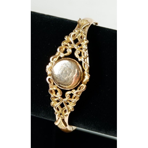 547 - A gold plated bangle with circular locket in scrollwork surround