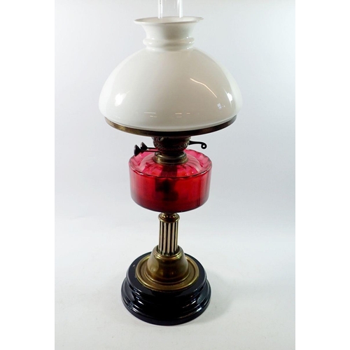 1316 - A Victorian brass oil lamp on black base with cranberry glass reservoir, 62cm