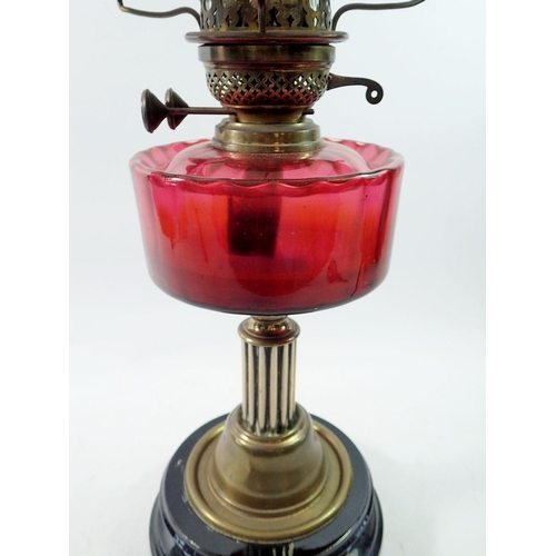 1316 - A Victorian brass oil lamp on black base with cranberry glass reservoir, 62cm