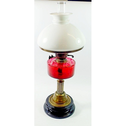 1186 - A Victorian brass oil lamp on black base with cranberry glass reservoir, 62cm