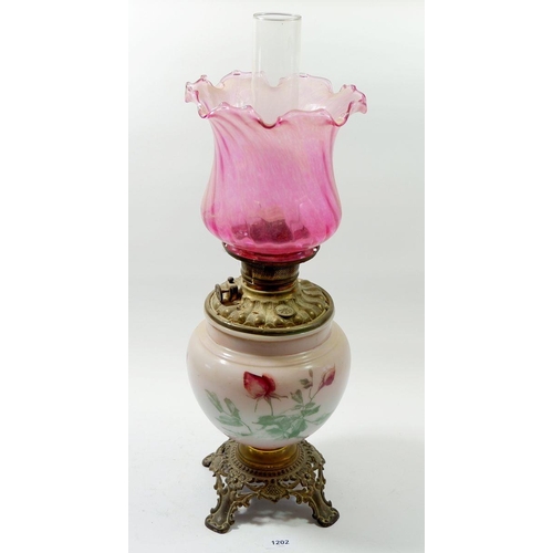 1202 - A Victorian brass mounted glass oil lamp printed roses with frilled cranberry shade