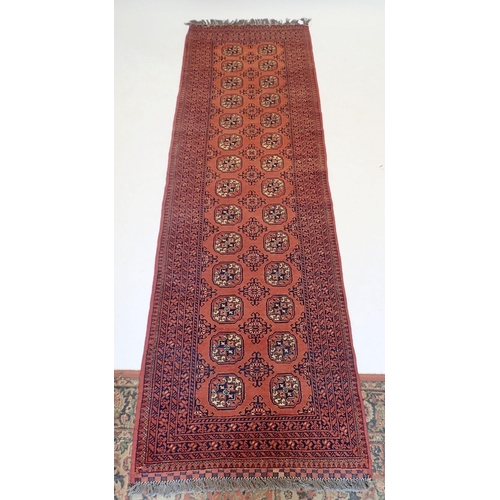 1192 - A Turkoman style runner with two rows of guls on madder ground, 289 x 87cm