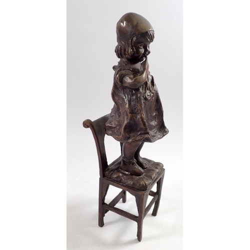 863 - A bronze figure of a child standing on a chair, 31cm tall