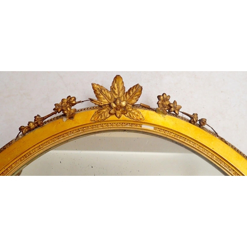 1086 - An antique oval gilt framed mirror with flower and leaf surmount, 73 x 57cm overall