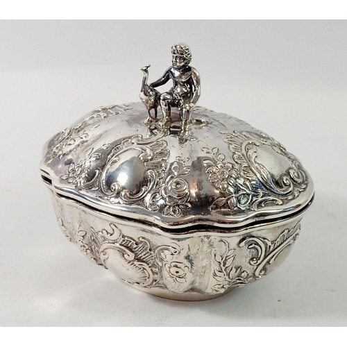 335 - A continental silver fluted oval box with putti and peacock finial and all over embossed scrollwork ... 