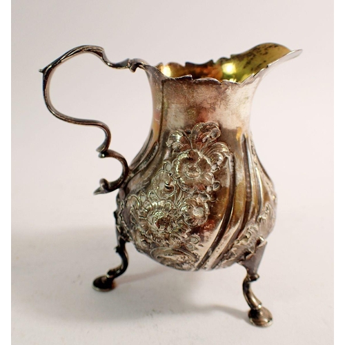 233 - A George III silver cream jug with embossed decoration, gilt interior and three hoof feet, 10cm tall... 