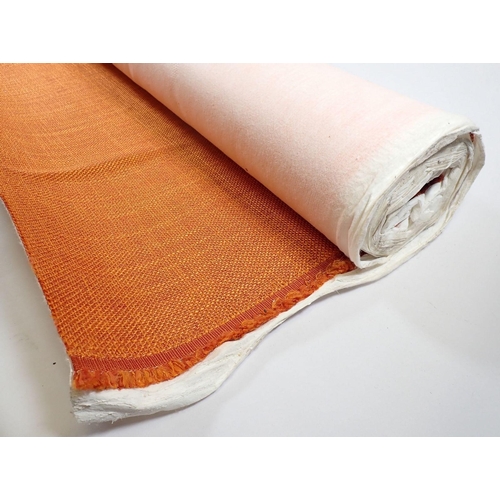 571 - An long piece of orange woven upholstery fabric on a roll