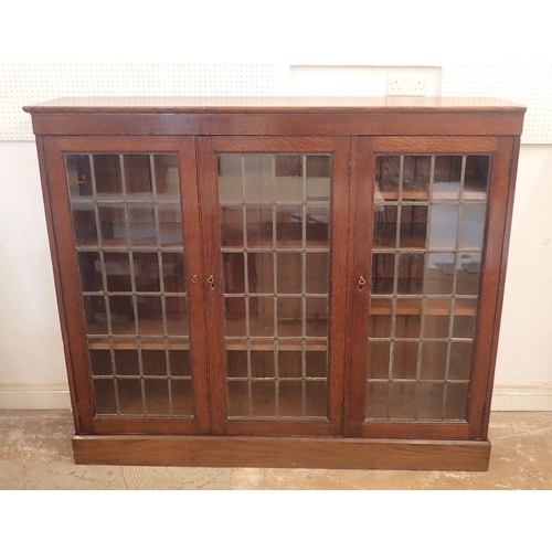 977 - An early 20th century oak lead glazed dwarf bookcase with three doors enclosing shelves, 156cm wide ... 