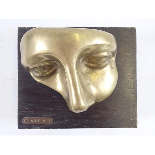 1082 - A Venetian brass face mask mounted on a wooden plinth, 'Aris A' 14 x 12cm