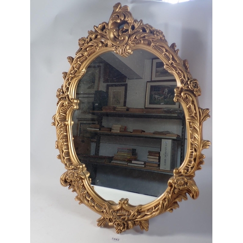 1443 - An oval gilt framed mirror with scrollwork decoration, 63cm tall