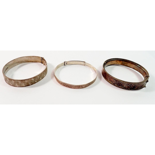 675 - A silver hinged bangle with geometric decoration and two other silver bangles, 55g