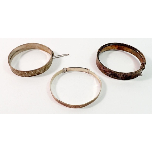 675 - A silver hinged bangle with geometric decoration and two other silver bangles, 55g