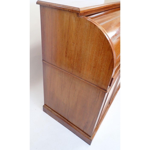 1057 - A Victorian walnut cylinder front desk with satinwood fitted interior all over cupboard on plinth ba... 