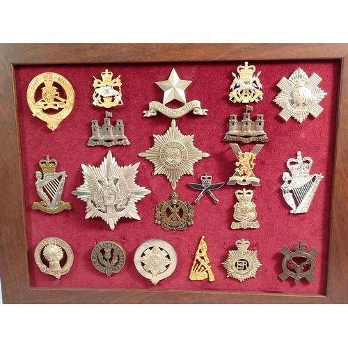 694 - A framed display of twenty one military cap badges and helmet plates including North Irish Brigade, ... 