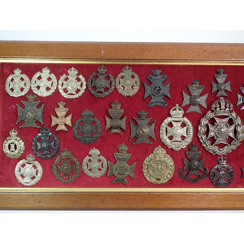 698 - A framed display of forty six military cap badges, helmet plates etc. including London, Queens Westm... 