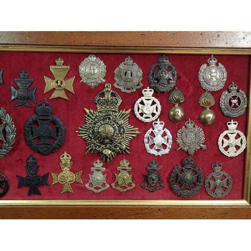 698 - A framed display of forty six military cap badges, helmet plates etc. including London, Queens Westm... 