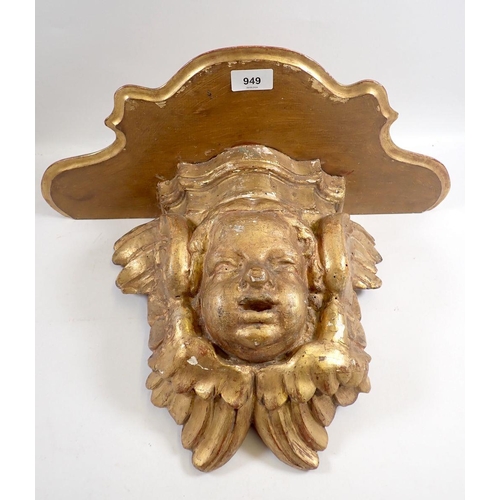 949 - An antique gilt carved wood cherub mask wall bracket with later shaped shelf above, 31cm high