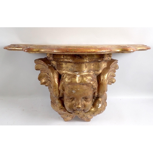 949 - An antique gilt carved wood cherub mask wall bracket with later shaped shelf above, 31cm high