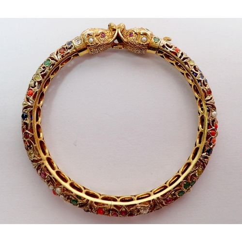 442 - A 9 carat gold Eastern pierced hinged bangle with elephant head terminals set semi precious stones, ... 